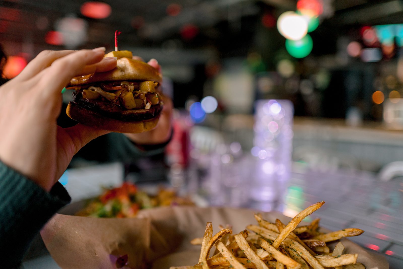A guest holding a burger above a table of food at 1129