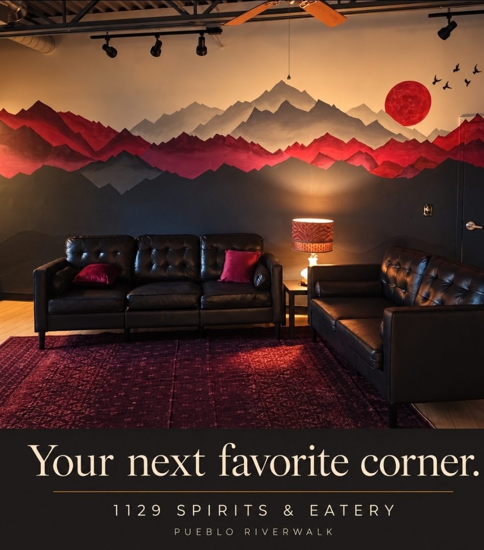 The Lounge at 1129 Spirits & Eatery: tufted leather sofas and a deep red patterned rug beneath a mountain mural with a red sun, framed by the words Your next favorite corner, 1129 Spirits & Eatery, Pueblo Riverwalk.